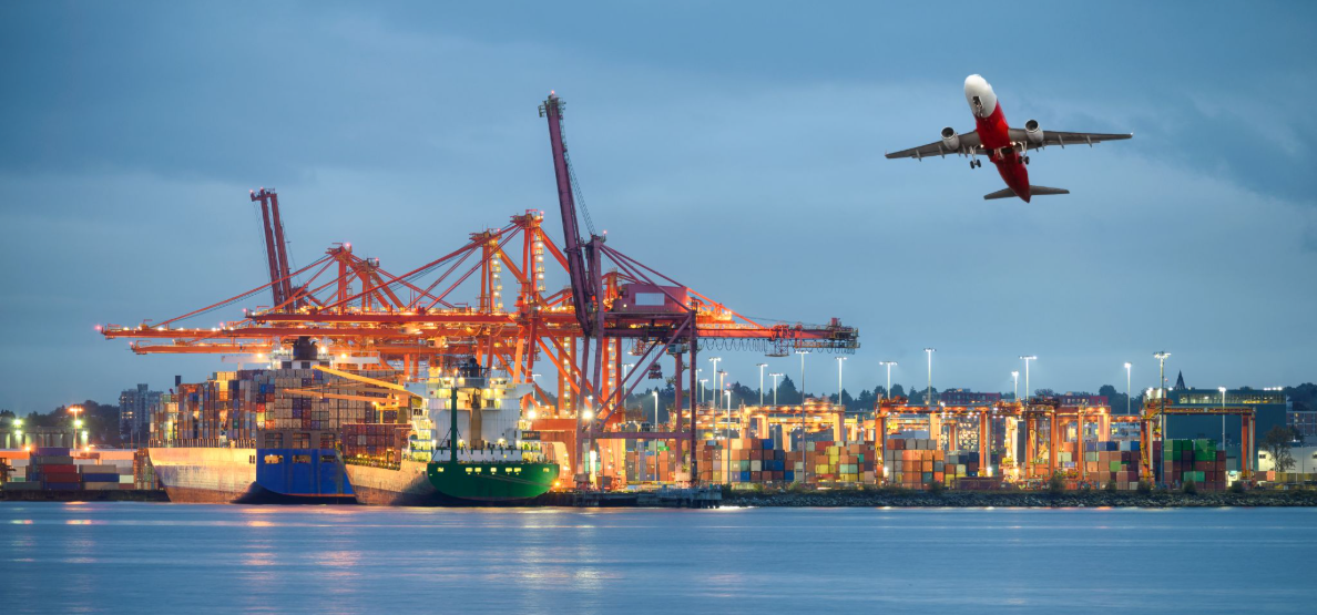 A cargo ship docked at a busy container port with cranes, while a commercial airplane takes off overhead in the evening. Traffic Consultants, Inc. (TCI)