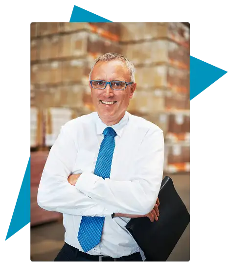 An older man in glasses and a blue tie stands with arms crossed, holding a folder, in a warehouse with stacked boxes in the background. Traffic Consultants, Inc. (TCI)