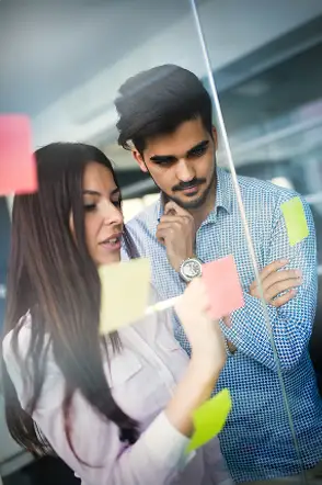 Two people stand by a glass wall with colorful sticky notes, discussing ideas in an office setting. Traffic Consultants, Inc. (TCI)